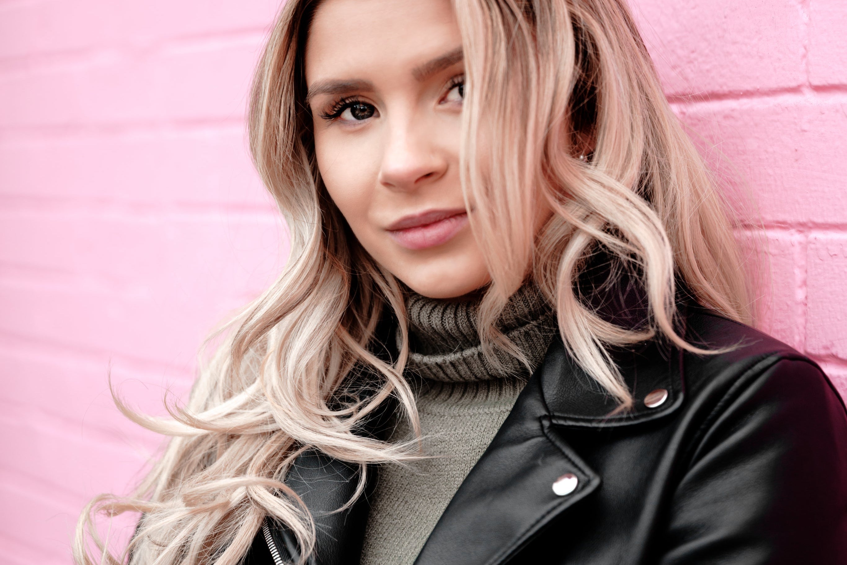 Person wearing a black leather jacket against a pink brick wall